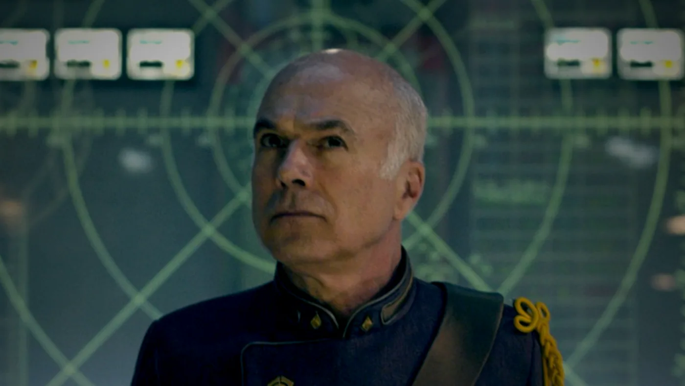 Marshal Wetherby in uniform before a wall of green tracking displays