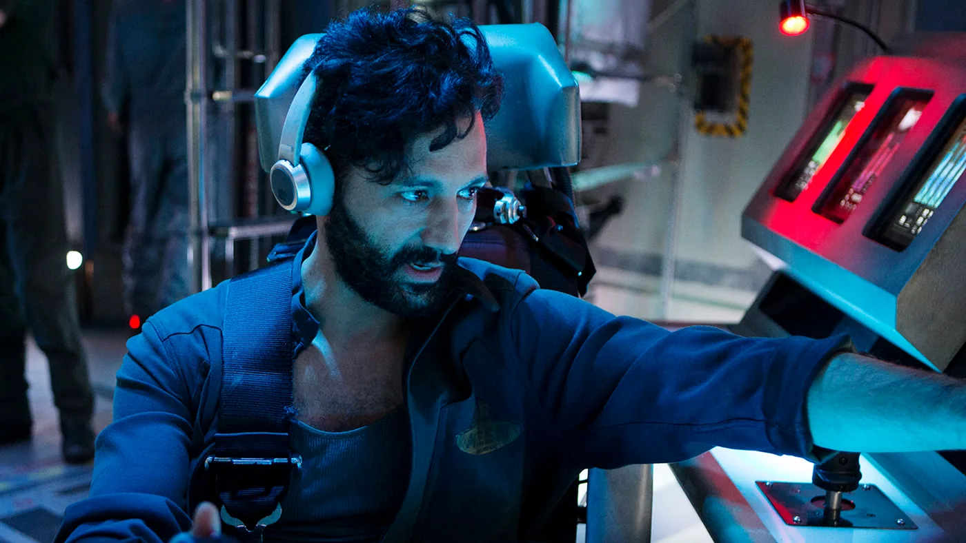 Viktor Gordon in a blue flight suit and headset, working the controls of a rover cab